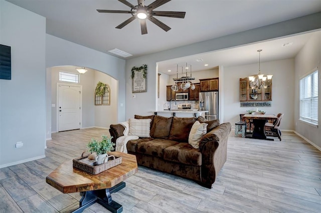 living room with visible vents, ceiling fan with notable chandelier, arched walkways, light wood finished floors, and baseboards