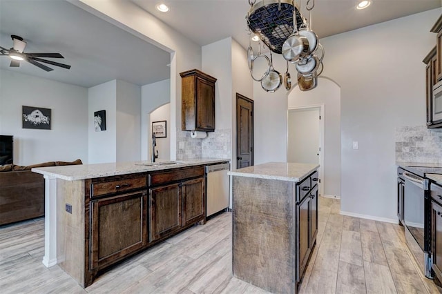 kitchen with light wood-style flooring, arched walkways, a sink, stainless steel appliances, and open floor plan