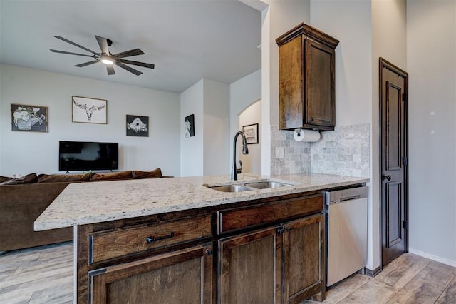kitchen featuring a sink, backsplash, arched walkways, light stone countertops, and dishwasher