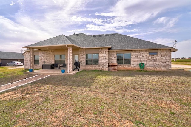rear view of house featuring a yard, brick siding, roof with shingles, and a patio area