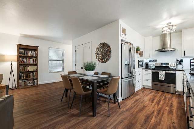 interior space featuring baseboards, wall chimney range hood, white cabinets, stainless steel appliances, and dark wood-style flooring