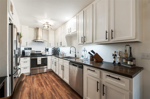 kitchen with a sink, stainless steel appliances, dark countertops, and wall chimney exhaust hood