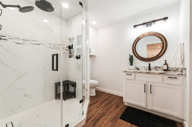 bathroom with a marble finish shower, baseboards, toilet, wood finished floors, and vanity