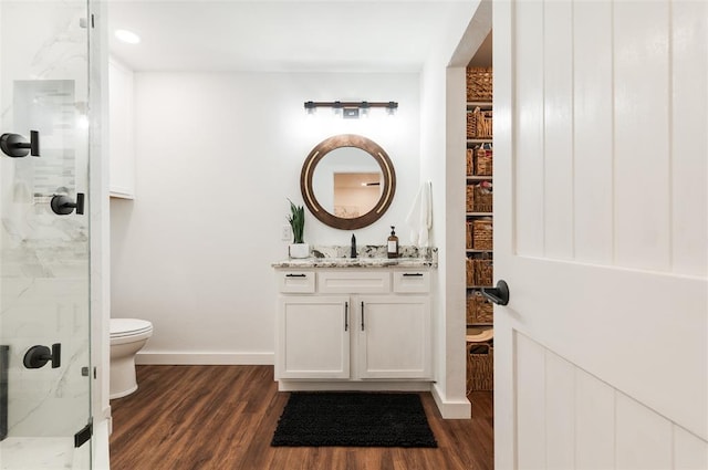 bathroom featuring toilet, wood finished floors, baseboards, and a marble finish shower