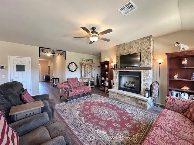 living area with visible vents, vaulted ceiling, a fireplace, wood finished floors, and a ceiling fan