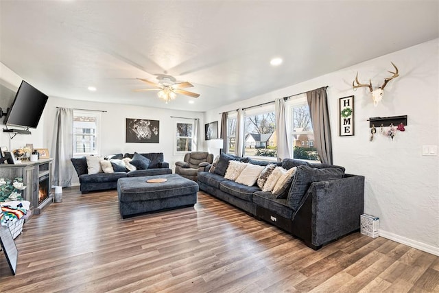 living area featuring a ceiling fan, wood finished floors, baseboards, recessed lighting, and a lit fireplace