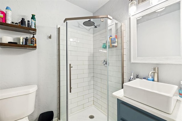 bathroom with a stall shower, toilet, vanity, and a textured wall