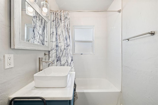 full bath with shower / tub combo with curtain, vanity, and a textured wall