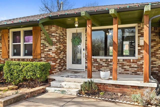 view of exterior entry featuring covered porch and brick siding