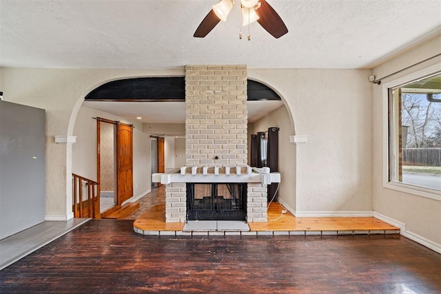 living room featuring baseboards, arched walkways, ceiling fan, hardwood / wood-style flooring, and a textured ceiling