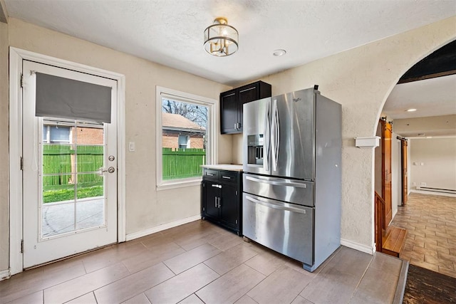 kitchen with arched walkways, stainless steel fridge, a textured wall, and dark cabinets