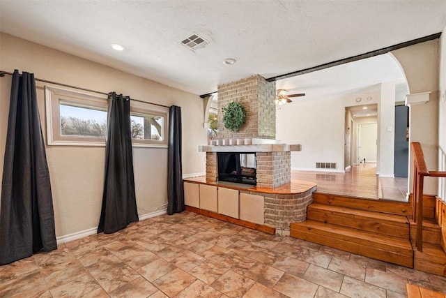 living room with visible vents, a textured ceiling, a fireplace, and a ceiling fan