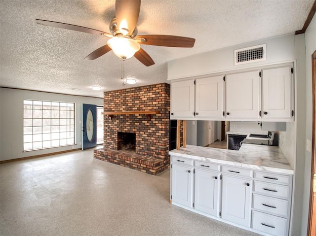 kitchen with visible vents, a textured ceiling, open floor plan, white cabinetry, and a brick fireplace