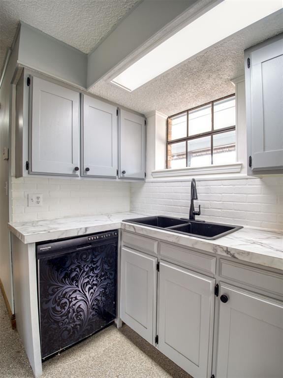 kitchen featuring dishwasher, a textured ceiling, tasteful backsplash, and a sink