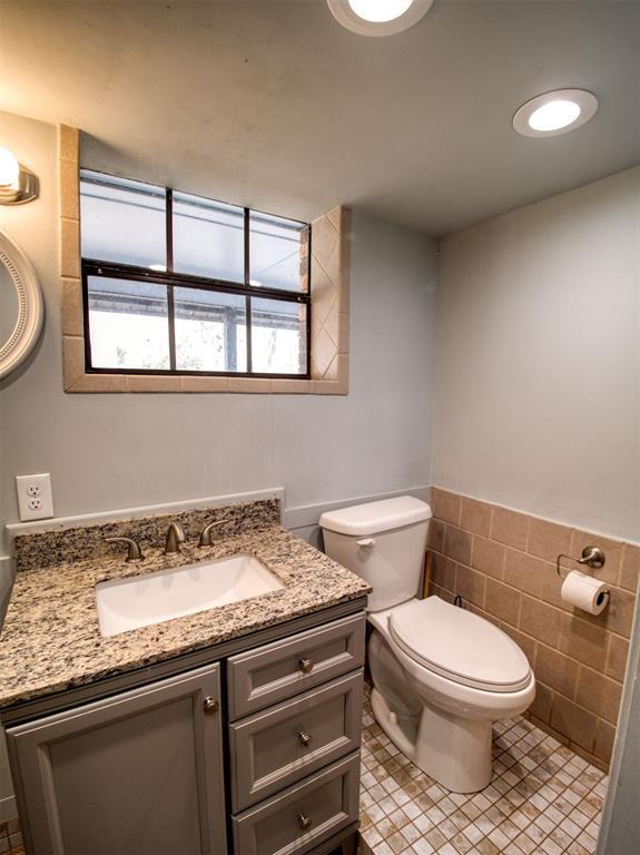 half bath with vanity, a wainscoted wall, tile walls, toilet, and tile patterned floors