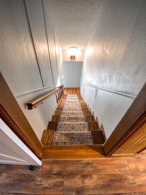 stairway with wood finished floors and a textured ceiling