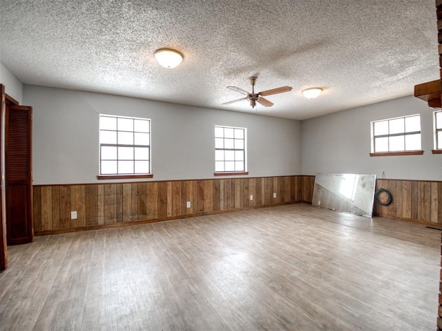 unfurnished room featuring wooden walls, wood finished floors, wainscoting, and a textured ceiling