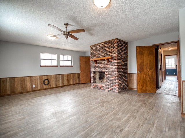 unfurnished living room with a ceiling fan, wood finished floors, a wainscoted wall, a fireplace, and a textured ceiling