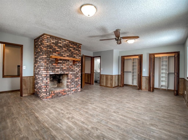 unfurnished living room featuring wainscoting, a brick fireplace, a textured ceiling, and wood finished floors