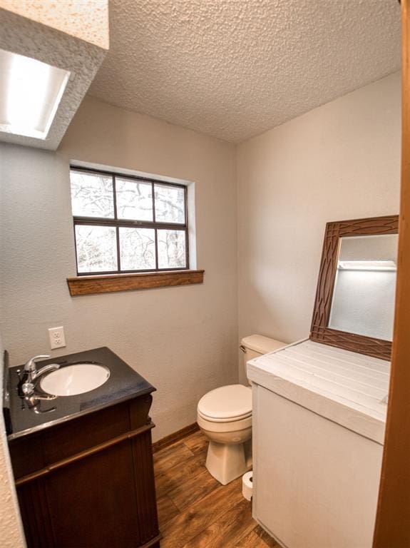 bathroom featuring toilet, a textured ceiling, wood finished floors, a skylight, and vanity