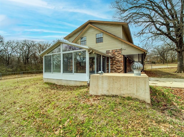 back of property featuring a yard, fence, brick siding, and a sunroom