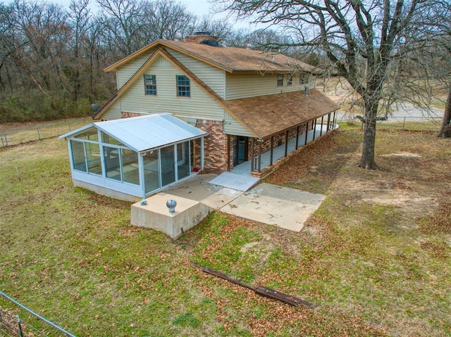 rear view of house featuring a lawn, fence, a sunroom, brick siding, and a chimney