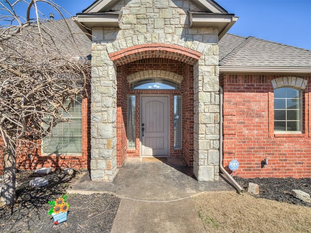 doorway to property featuring brick siding, stone siding, and roof with shingles