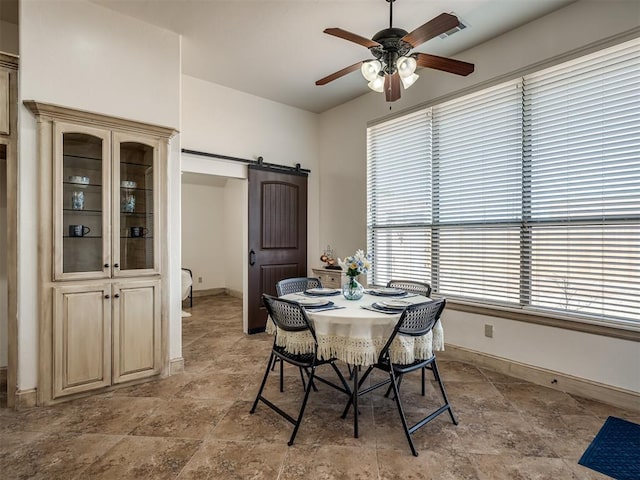 dining room featuring baseboards, a ceiling fan, stone finish flooring, and a barn door