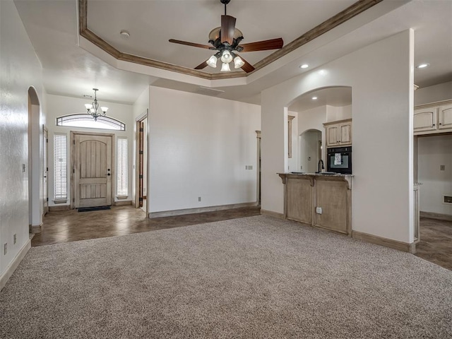 unfurnished living room with light carpet, arched walkways, baseboards, and a tray ceiling