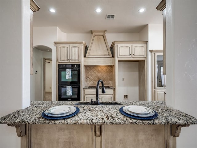 kitchen featuring a sink, visible vents, light stone countertops, and dobule oven black