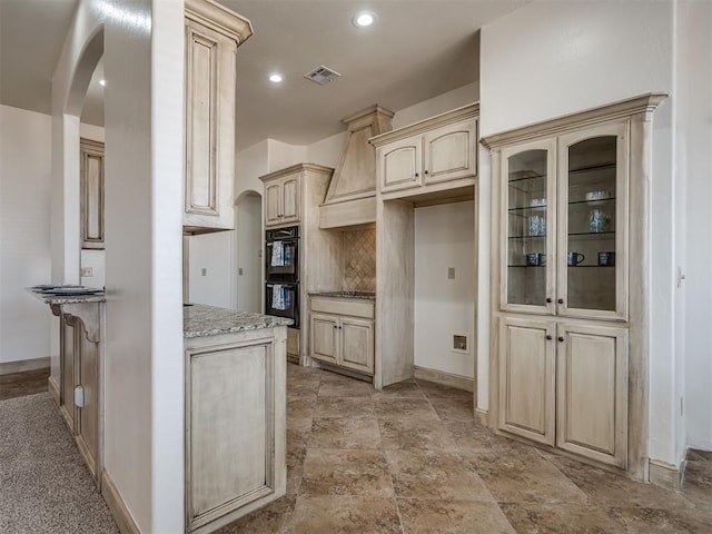 kitchen featuring visible vents, light stone countertops, backsplash, and arched walkways