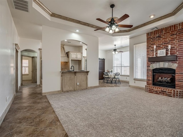 living room featuring visible vents, a raised ceiling, arched walkways, and a fireplace