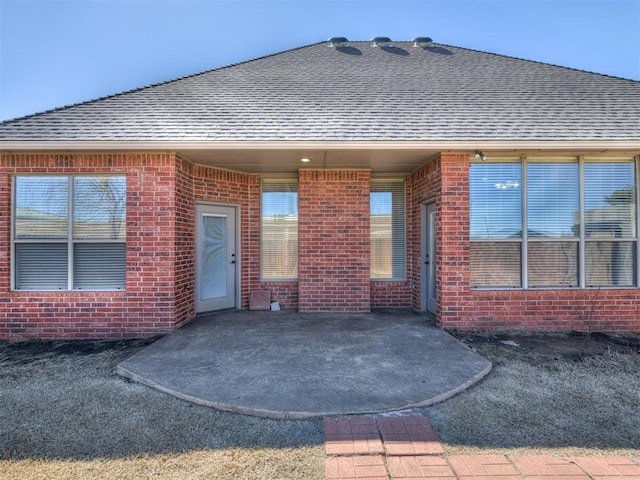 rear view of house with a patio, brick siding, and a shingled roof