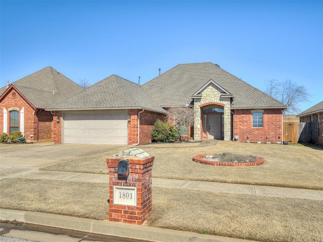 view of front of property featuring roof with shingles, an attached garage, concrete driveway, stone siding, and brick siding