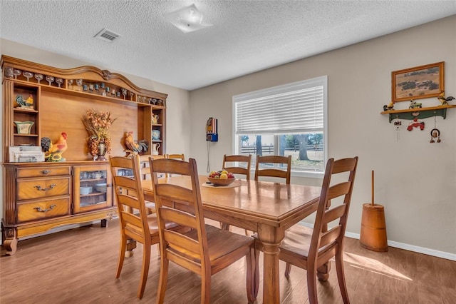 dining space featuring a textured ceiling, wood finished floors, visible vents, and baseboards