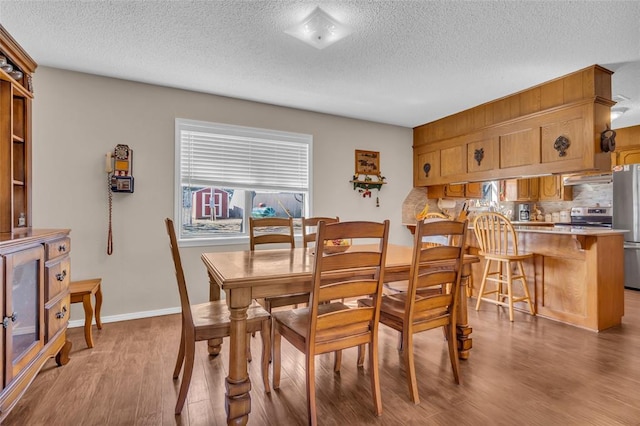 dining room featuring light wood-style floors, baseboards, and a textured ceiling