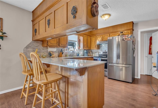 kitchen with visible vents, under cabinet range hood, stainless steel appliances, a peninsula, and light wood finished floors