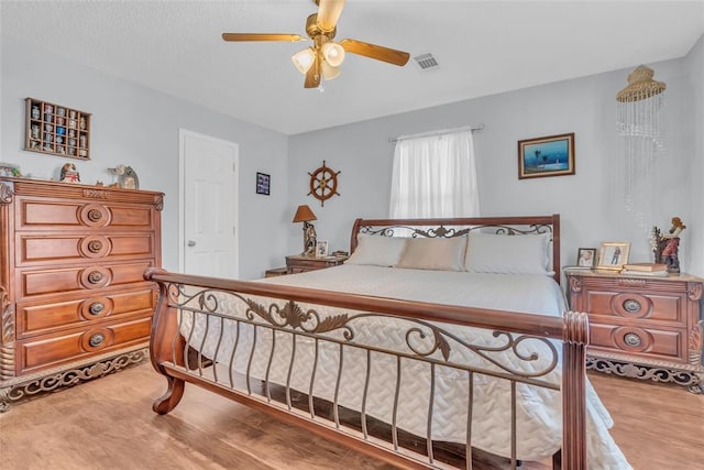 bedroom with visible vents, a textured ceiling, wood finished floors, and a ceiling fan