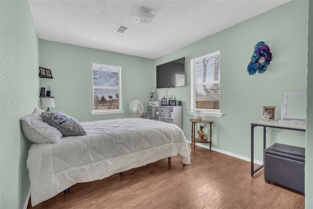 bedroom with baseboards, wood finished floors, visible vents, and a textured ceiling