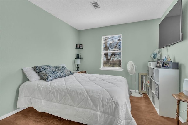 bedroom with baseboards, wood finished floors, visible vents, and a textured ceiling