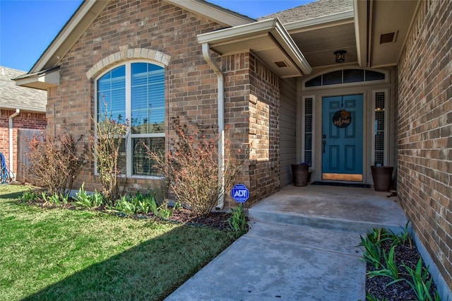 entrance to property featuring a yard, brick siding, and a shingled roof