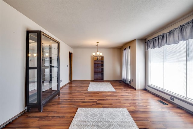 interior space with a notable chandelier, wood finished floors, baseboards, and a textured ceiling