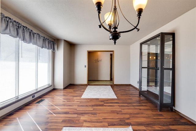 interior space with a notable chandelier, wood finished floors, a baseboard radiator, and a textured ceiling