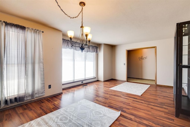 unfurnished dining area with baseboards, a textured ceiling, an inviting chandelier, and wood finished floors