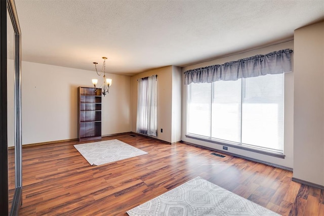 interior space with visible vents, baseboards, a chandelier, wood finished floors, and a textured ceiling