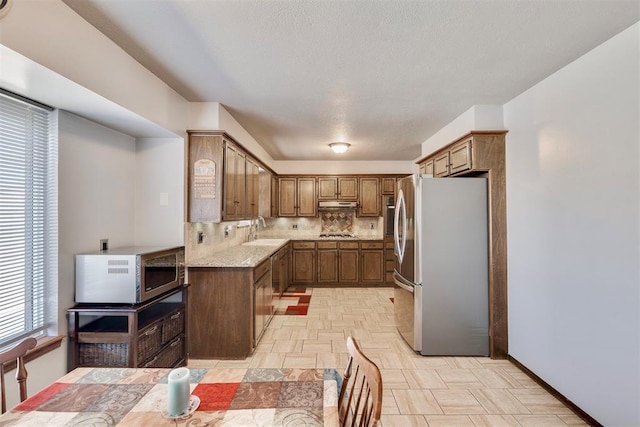 kitchen with a sink, light stone counters, under cabinet range hood, tasteful backsplash, and stainless steel appliances