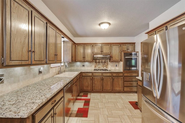 kitchen with a sink, decorative backsplash, stainless steel appliances, under cabinet range hood, and brown cabinets