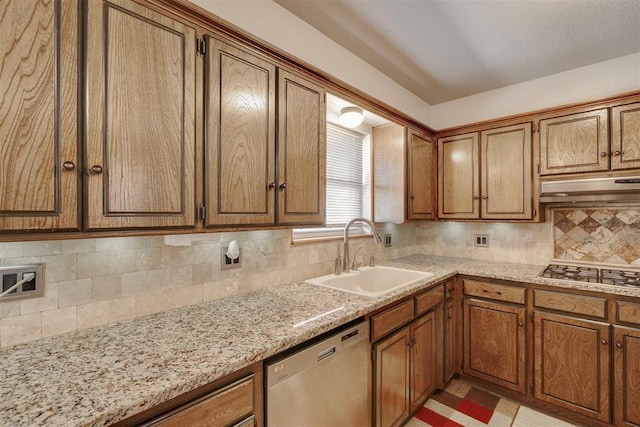 kitchen with brown cabinets, under cabinet range hood, a sink, tasteful backsplash, and appliances with stainless steel finishes