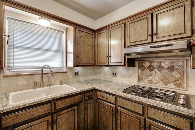 kitchen featuring under cabinet range hood, backsplash, stainless steel gas cooktop, and a sink