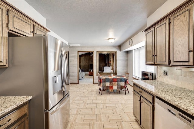 kitchen with dishwashing machine, light stone countertops, stainless steel refrigerator with ice dispenser, and a textured ceiling